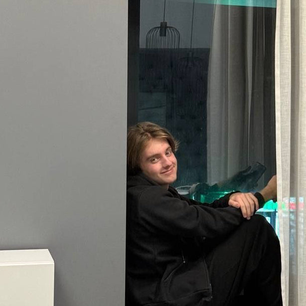 Dmitry Volkov sitting inside a small room with gray walls and white curtains.
